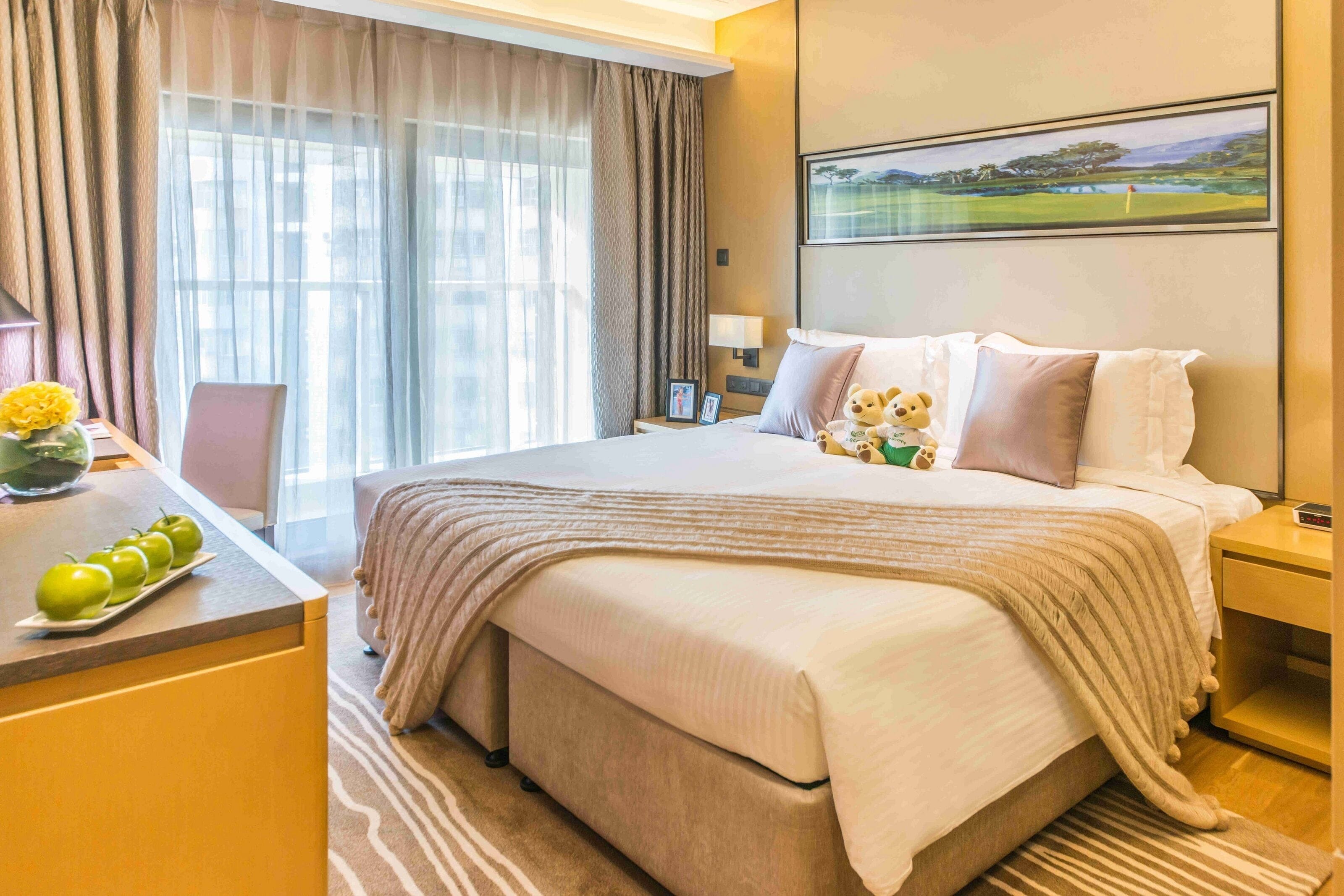 A hotel room with a large bed, a desk with a vase of flowers, and a painting on the wall.