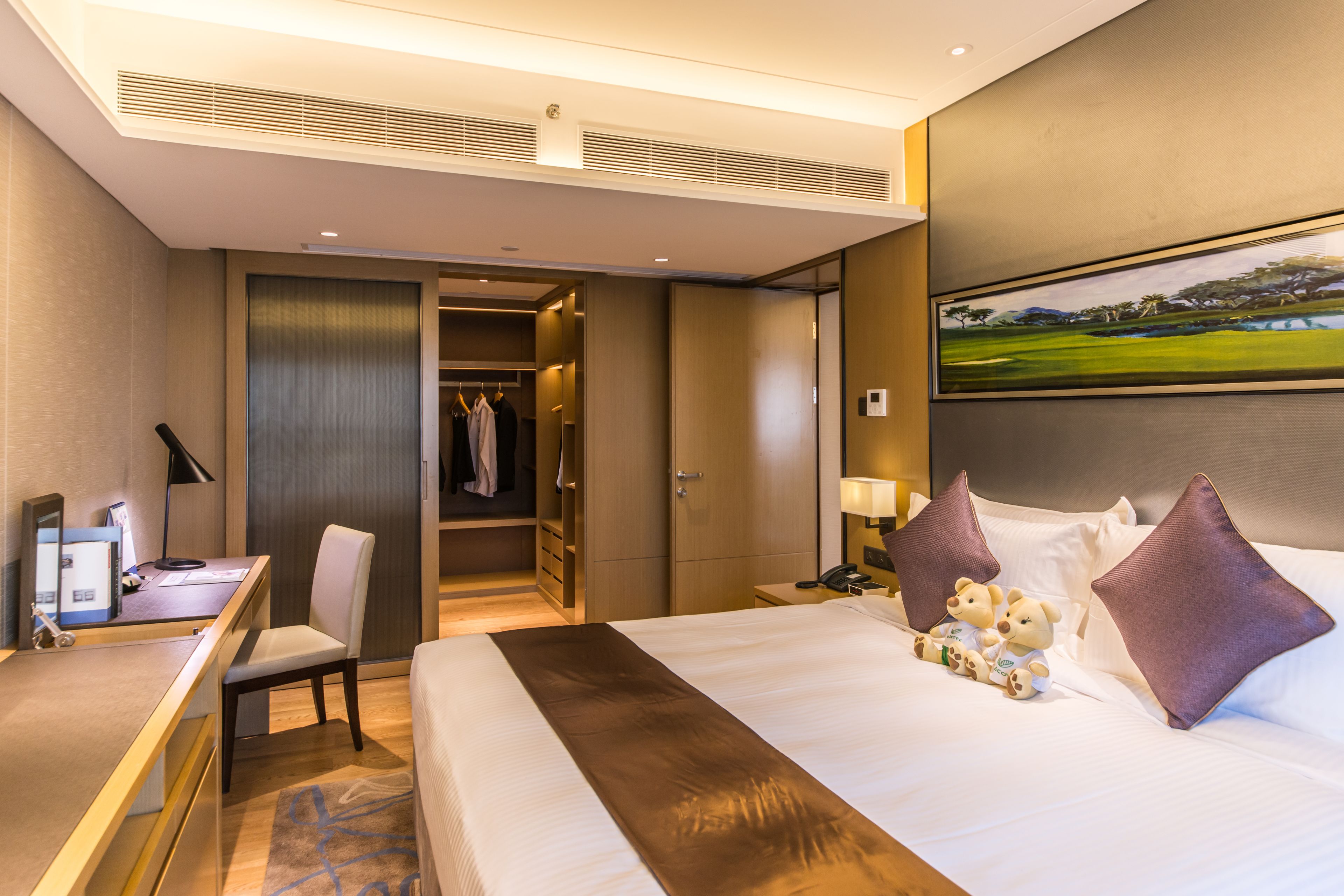 A hotel room with a bed, a desk, a chair, a wardrobe, and a painting on the wall.