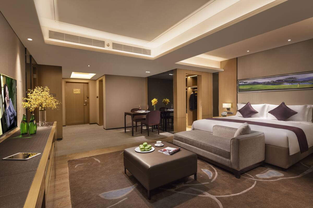 A hotel room with a bed, a sofa, a dining table, and a TV.