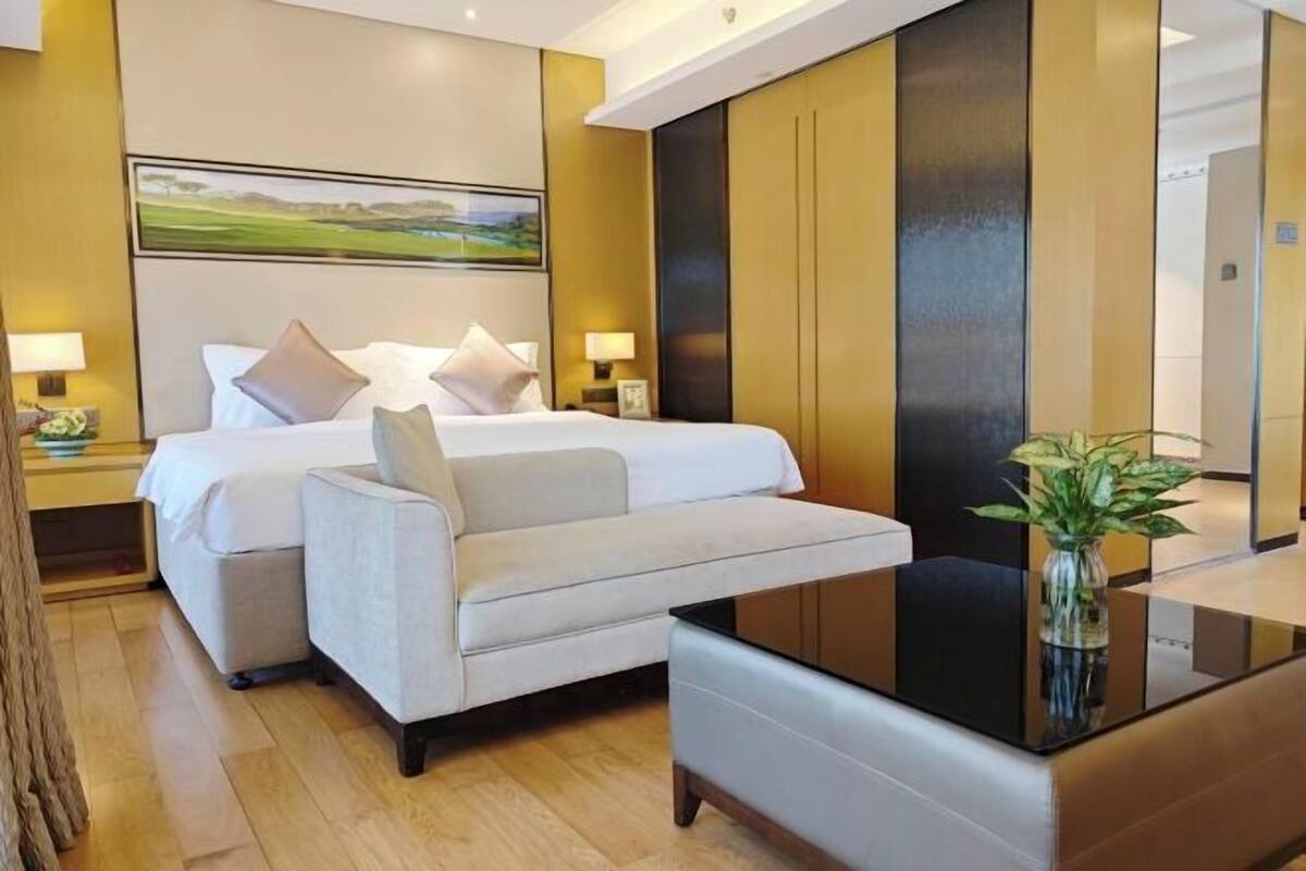 A hotel room with a bed, two bedside tables, a sofa, a coffee table, and a painting on the wall.