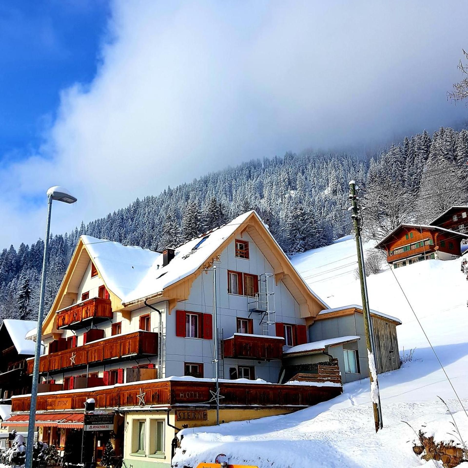 A multi-story hotel with a snow-covered roof and balconies, set against a backdrop of a snowy mountain.