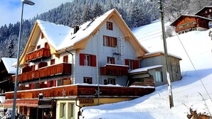 Ett hotell med flera våningar, ett snötäckt tak och balkonger, med ett snöigt berg i bakgrunden.