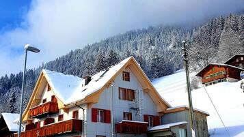 A multi-story hotel with a snow-covered roof and balconies, set against a backdrop of a snowy mountain.