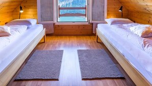 Ett mysigt sovrum på vinden med två sängar, ett stort fönster och utsikt över bergen.
