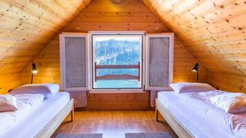 A cozy attic bedroom with two beds, a large window, and a view of mountains.