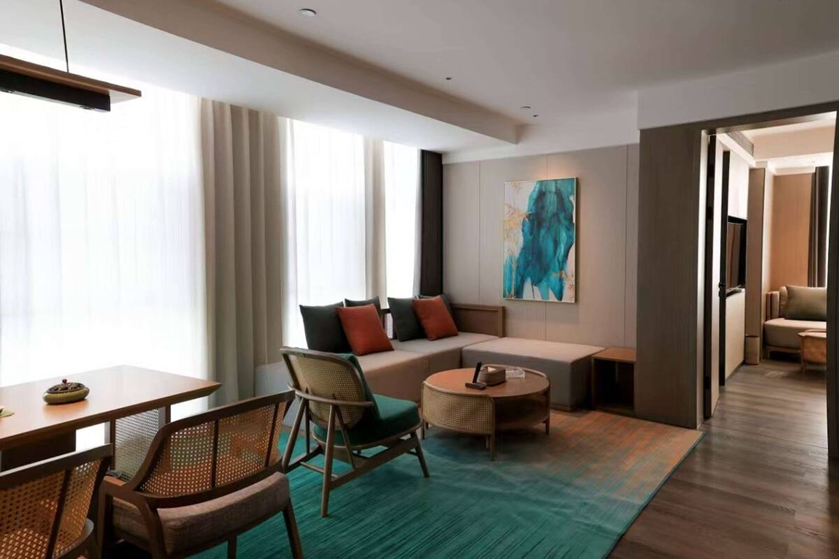 Une chambre d’hôtel moderne, équipée d’un canapé, de fauteuils, d’une petite table et d’une grande fenêtre avec des rideaux.