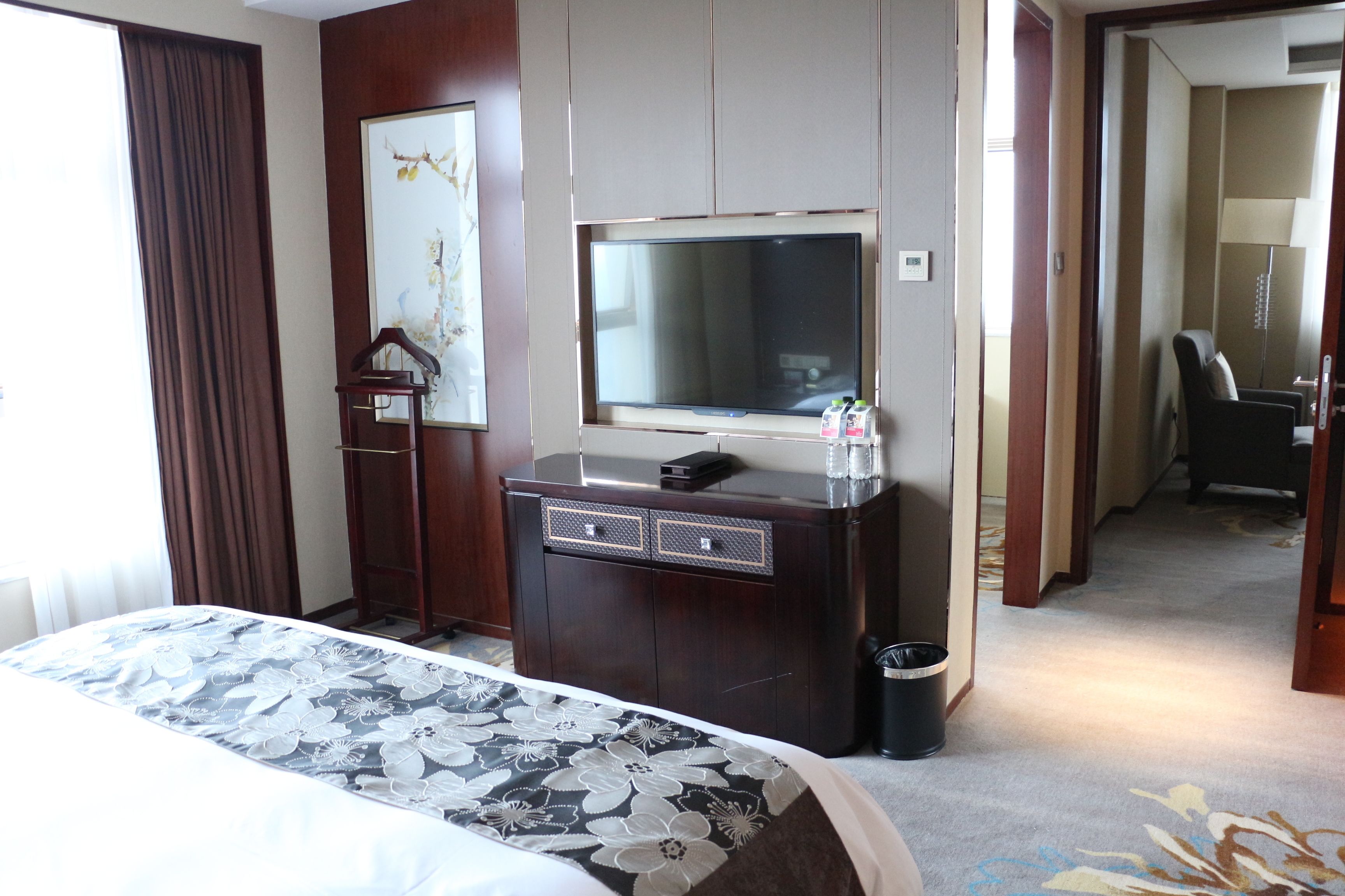 A hotel room with a bed, a TV on a wooden cabinet, a desk, and a trash can.