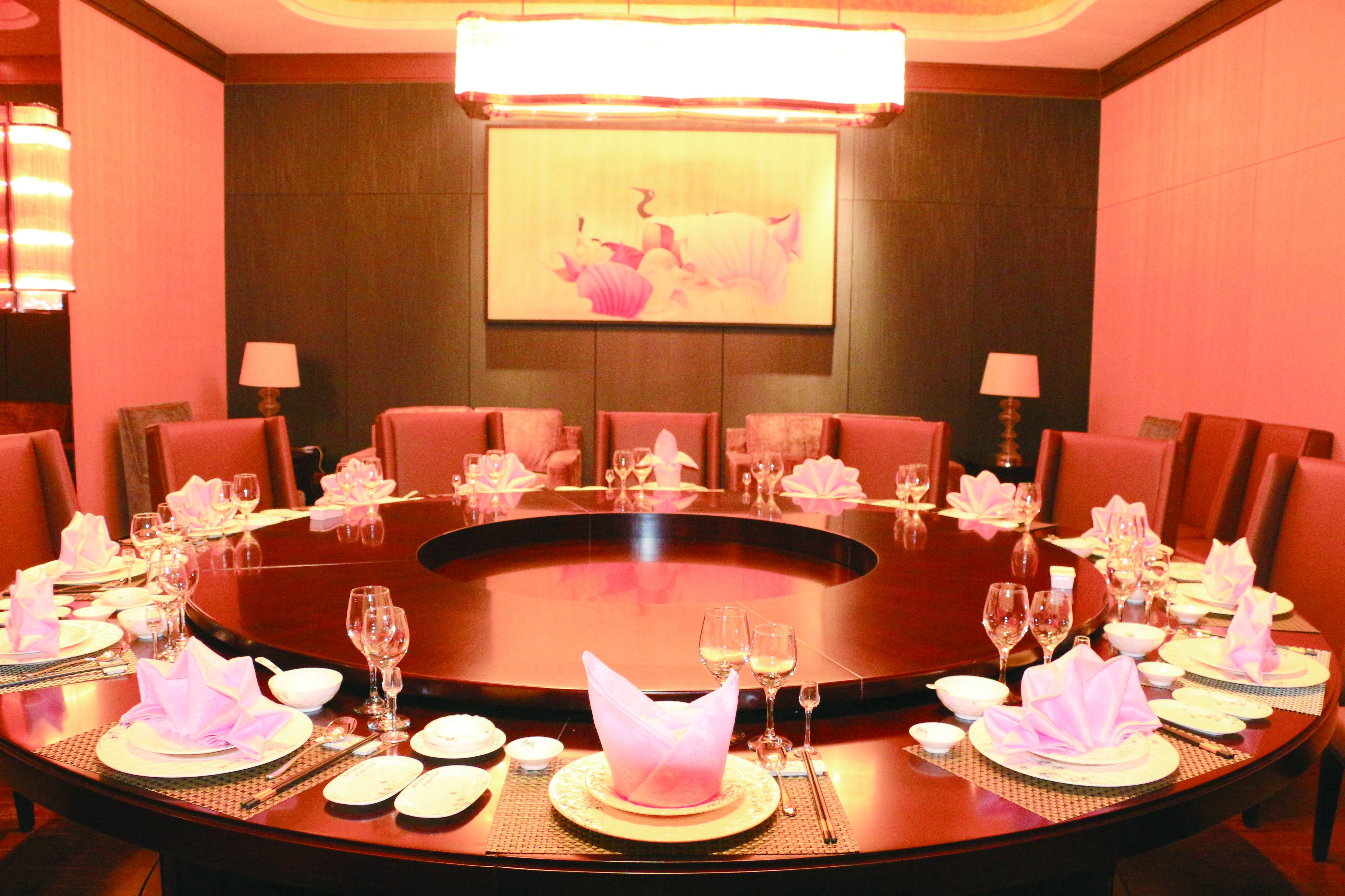 Un salón de conferencias con una mesa redonda dispuesta para una reunión, equipado con sillas, mesas y una pantalla grande.
