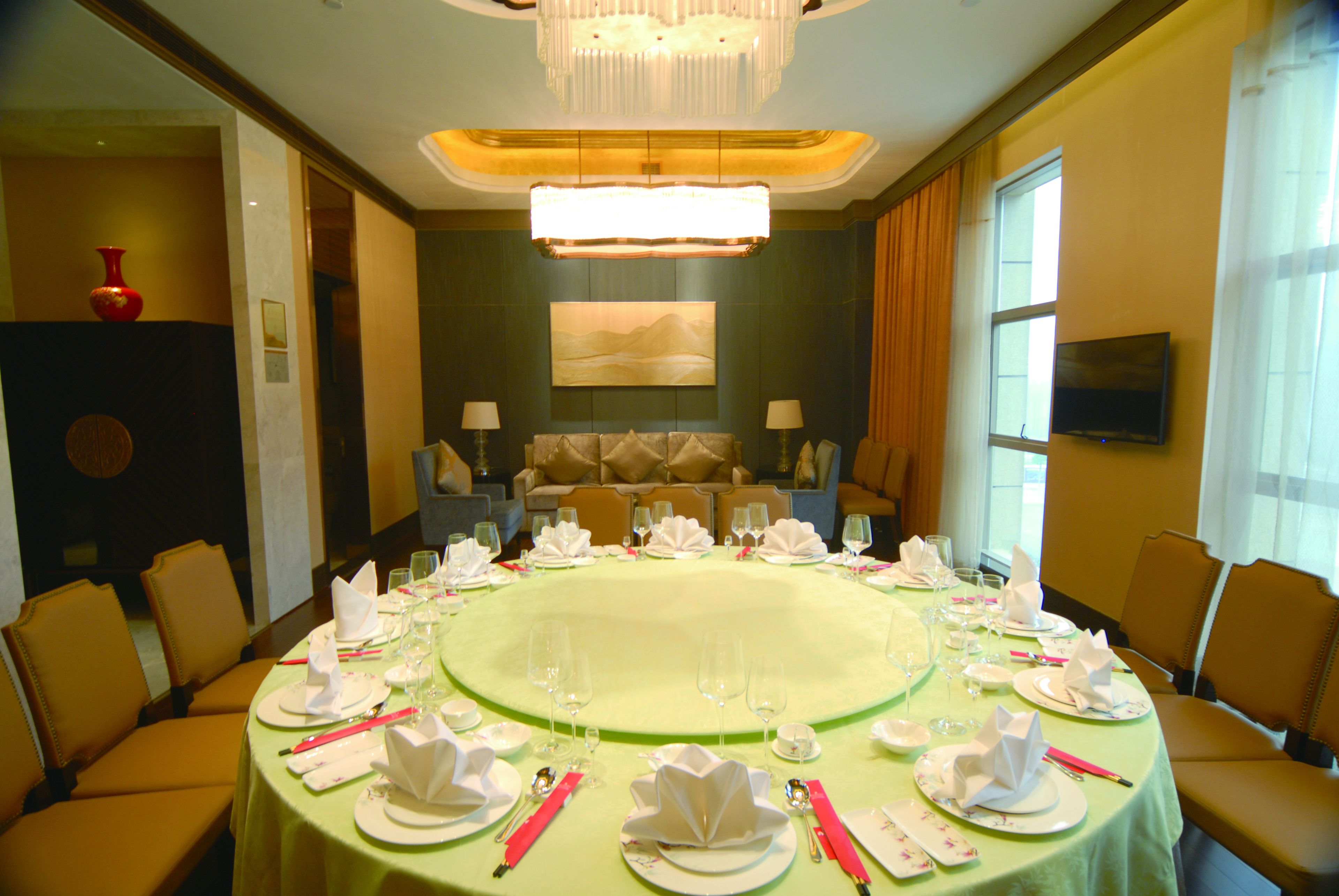 A conference room with a round table set for a meeting, equipped with chairs, a chandelier, and a television on the wall.