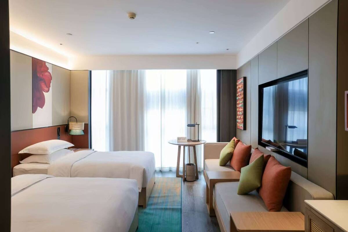 Une chambre d’hôtel avec deux lits, un canapé, une télévision et une fenêtre avec des rideaux.