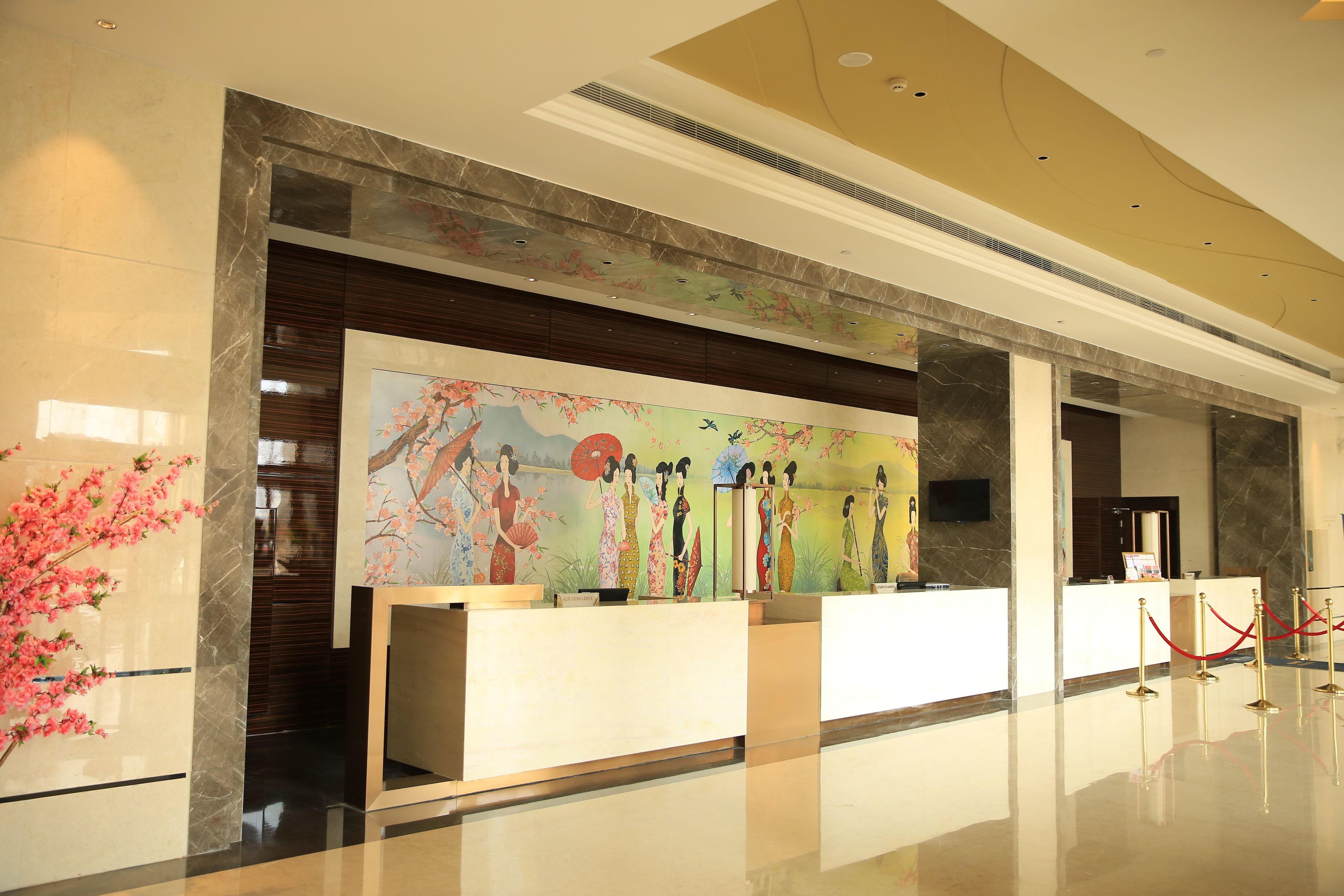 Una zona de recepción con un mostrador de mármol, un mural con figuras tradicionales y una barrera de cuerda roja.