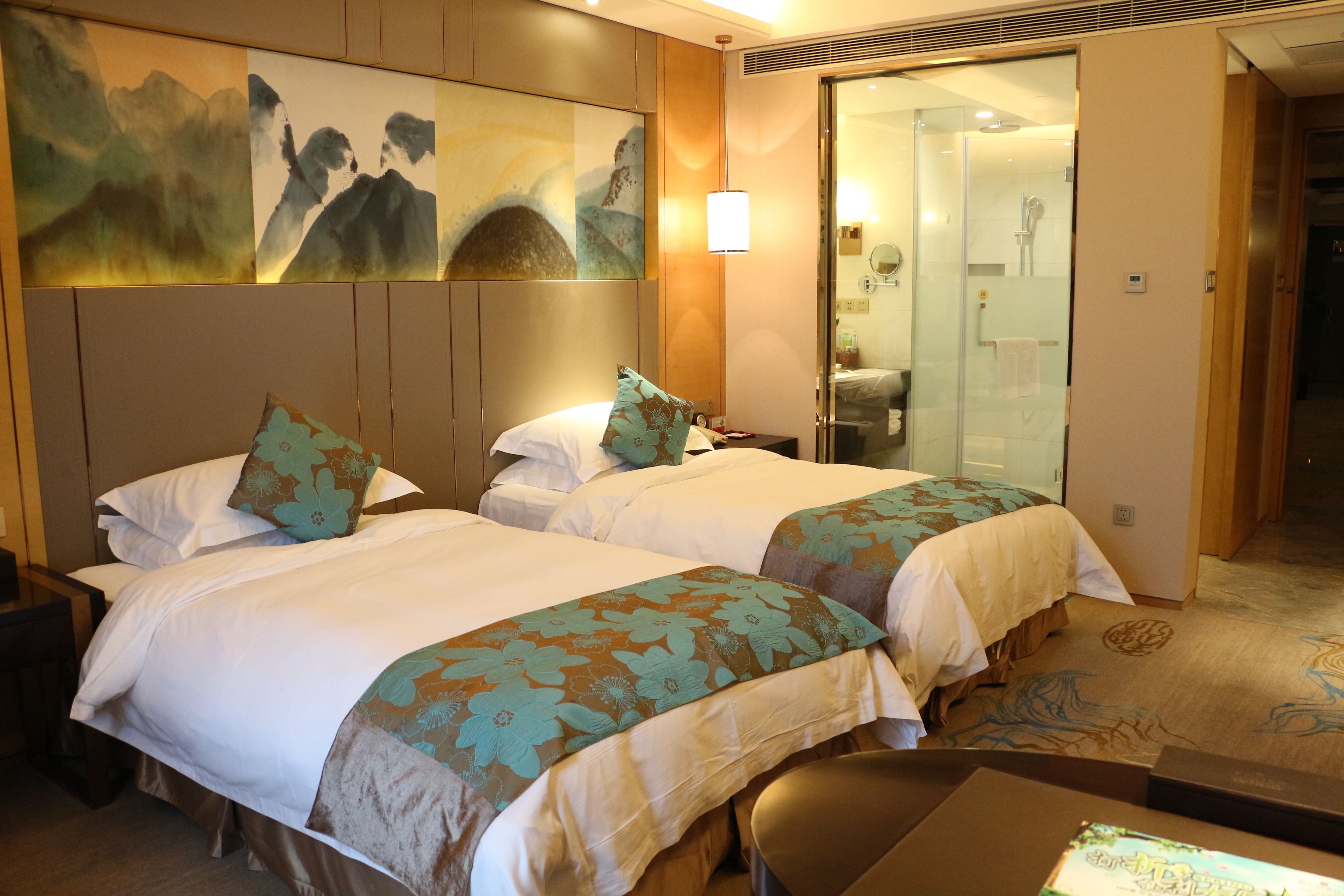 A hotel room with two beds, a desk, and a bathroom visible through a glass door.