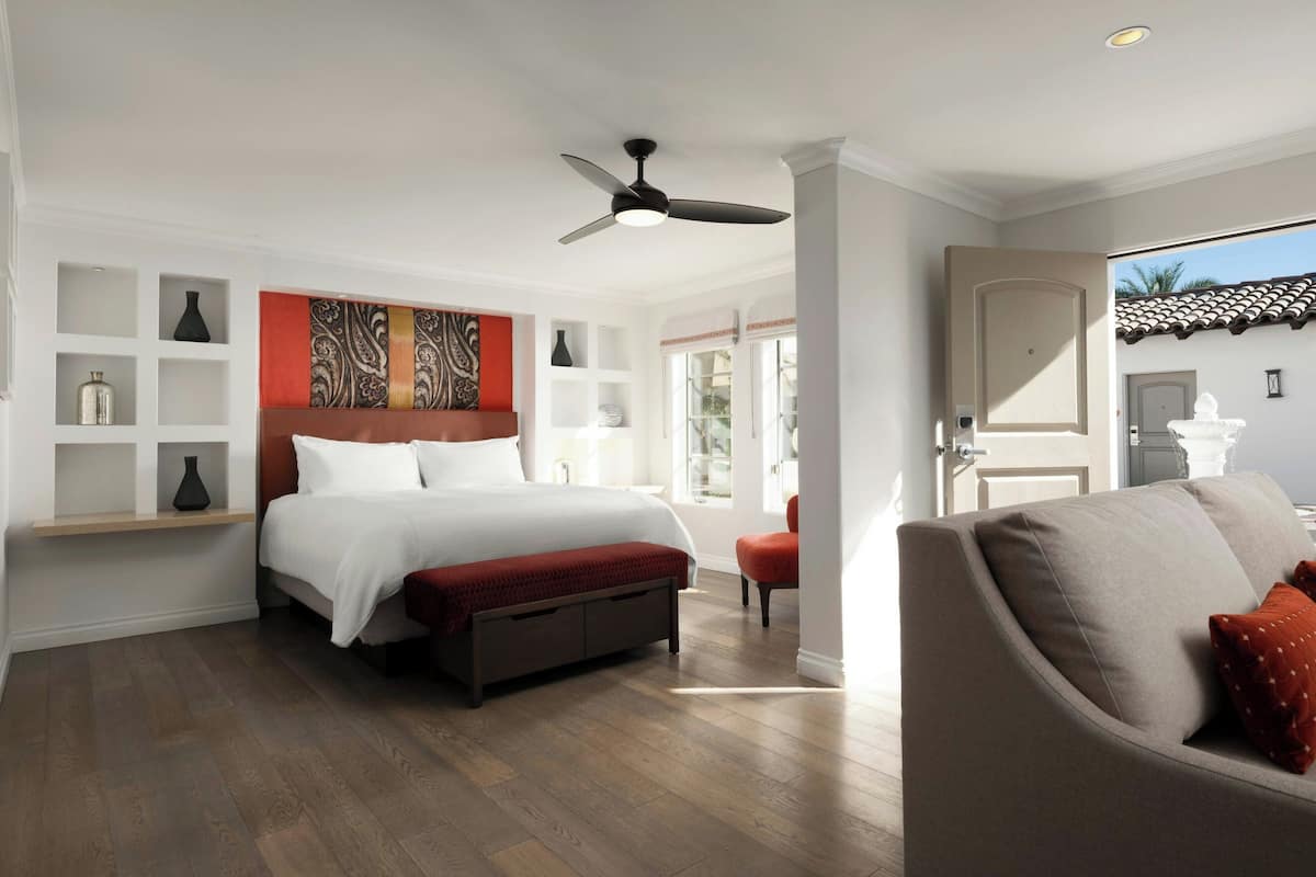A modern bedroom with a large bed, a ceiling fan, and a view of the outside.