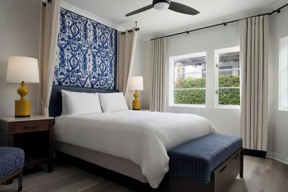 A neatly arranged bedroom with a bed, bedside tables, a bench, and a window with curtains.