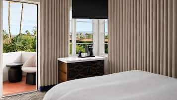 A hotel room with a bed, a desk with a coffee maker, a chair, and a TV.