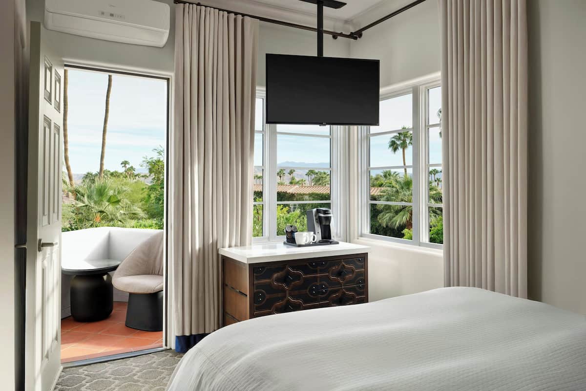 A hotel room with a bed, a desk with a coffee maker, a chair, and a TV.
