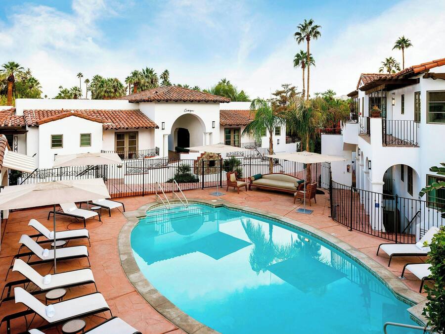 A pool area with lounge chairs and umbrellas, surrounded by white buildings with red-tiled roofs.