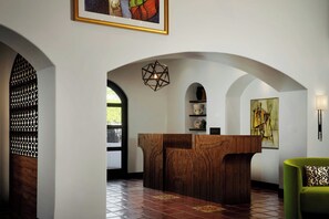 A reception area with a wooden reception desk, arched doorways, and a geometric pendant light. - Triada Palm Springs, Autograph Collection by Marriott (Palm Springs)