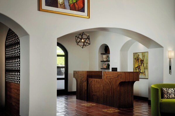 A reception area with a wooden reception desk, arched doorways, and a geometric pendant light.