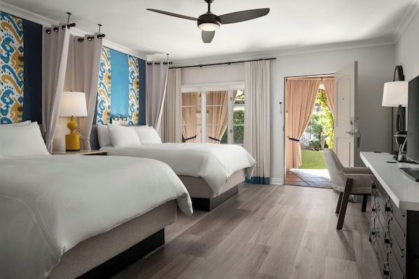 A hotel room with two beds, a ceiling fan, a desk with a lamp, and a view of the outdoors.