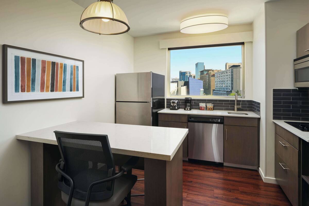 A modern kitchen with a dining area, stainless steel appliances, and a city view.