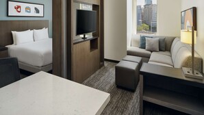 A hotel room with a bed, a TV mounted on a wooden panel, a sofa, a small table, and a window with a city view. - Hyatt House Atlanta Downtown (Atlanta)