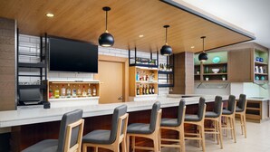 A modern kitchen with a bar area, wooden cabinets, a flat-screen TV, and bar stools. - Hyatt House Atlanta Downtown (Atlanta)
