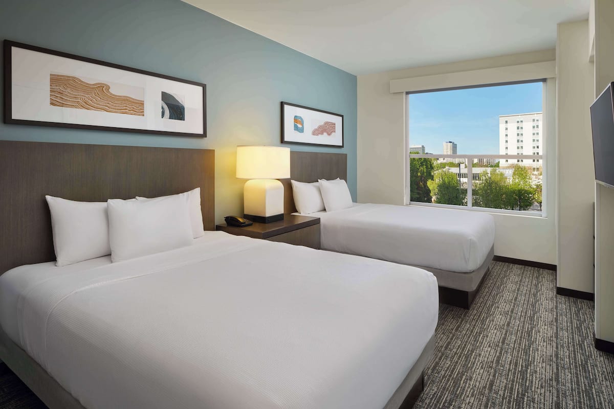 A hotel room with two beds, a nightstand with a lamp, and framed artwork on the wall.