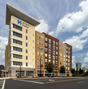 Un hotel de varios pisos con un llamativo letrero de 'Hyatt House', un acceso cubierto y un estacionamiento al frente.