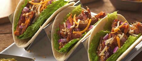 Three tacos with lettuce, shredded cheese, and red onions on a white tray.