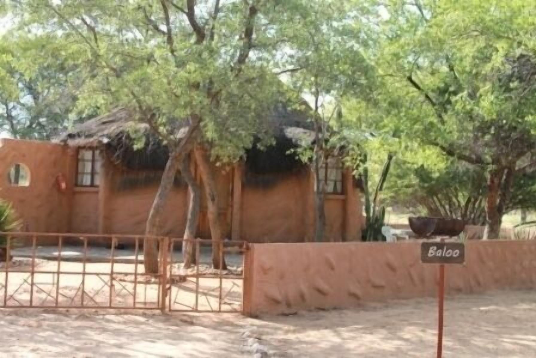 Una construcción rústica con techo de paja, rodeada de árboles y un área cercada.