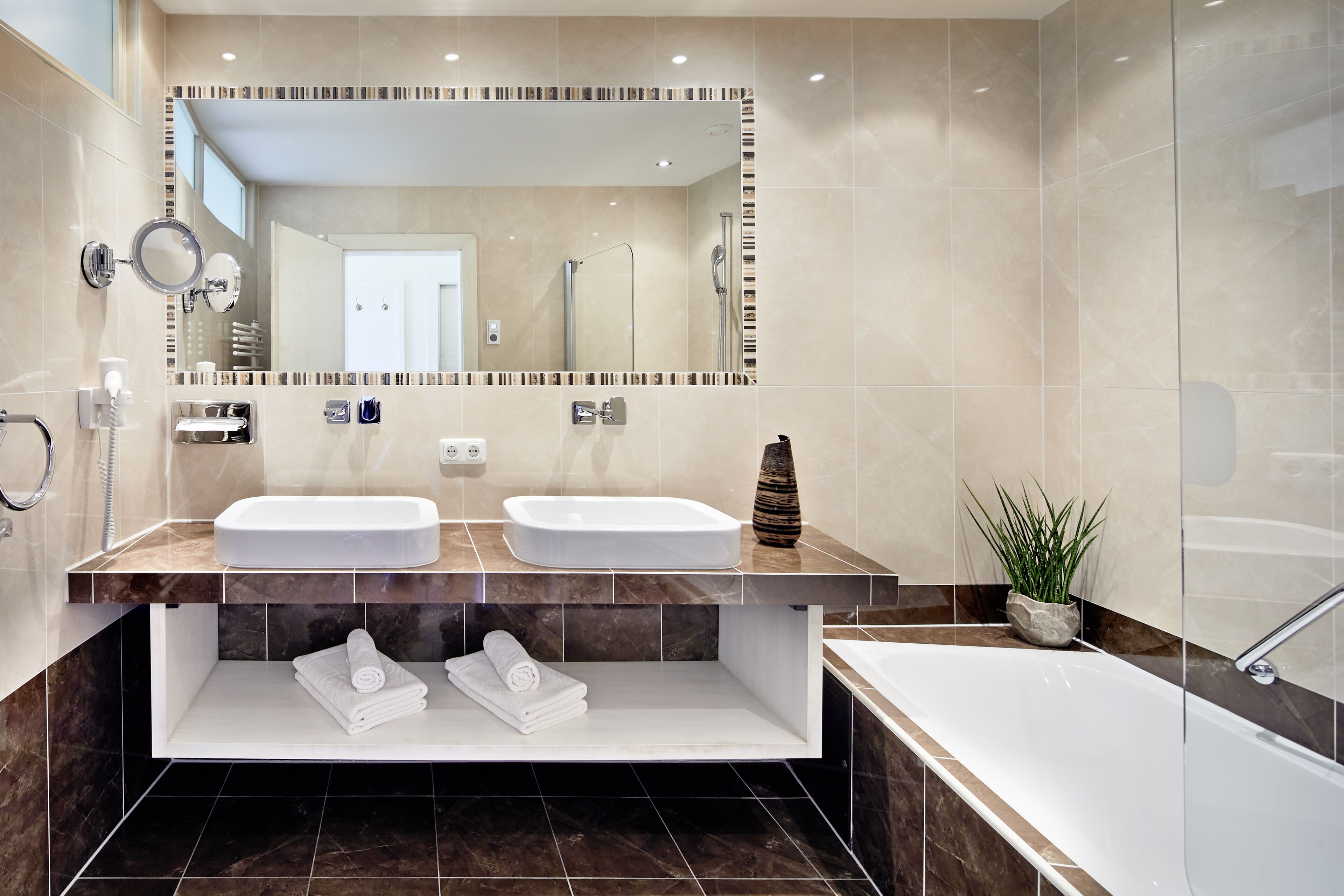Une salle de bain moderne avec deux lavabos, un grand miroir, une baignoire et une douche.