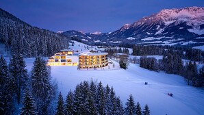 A snow-covered mountain resort with a multi-story building featuring balconies and a ski slope in the background. - Hotel Kaiserhof (Ellmau)