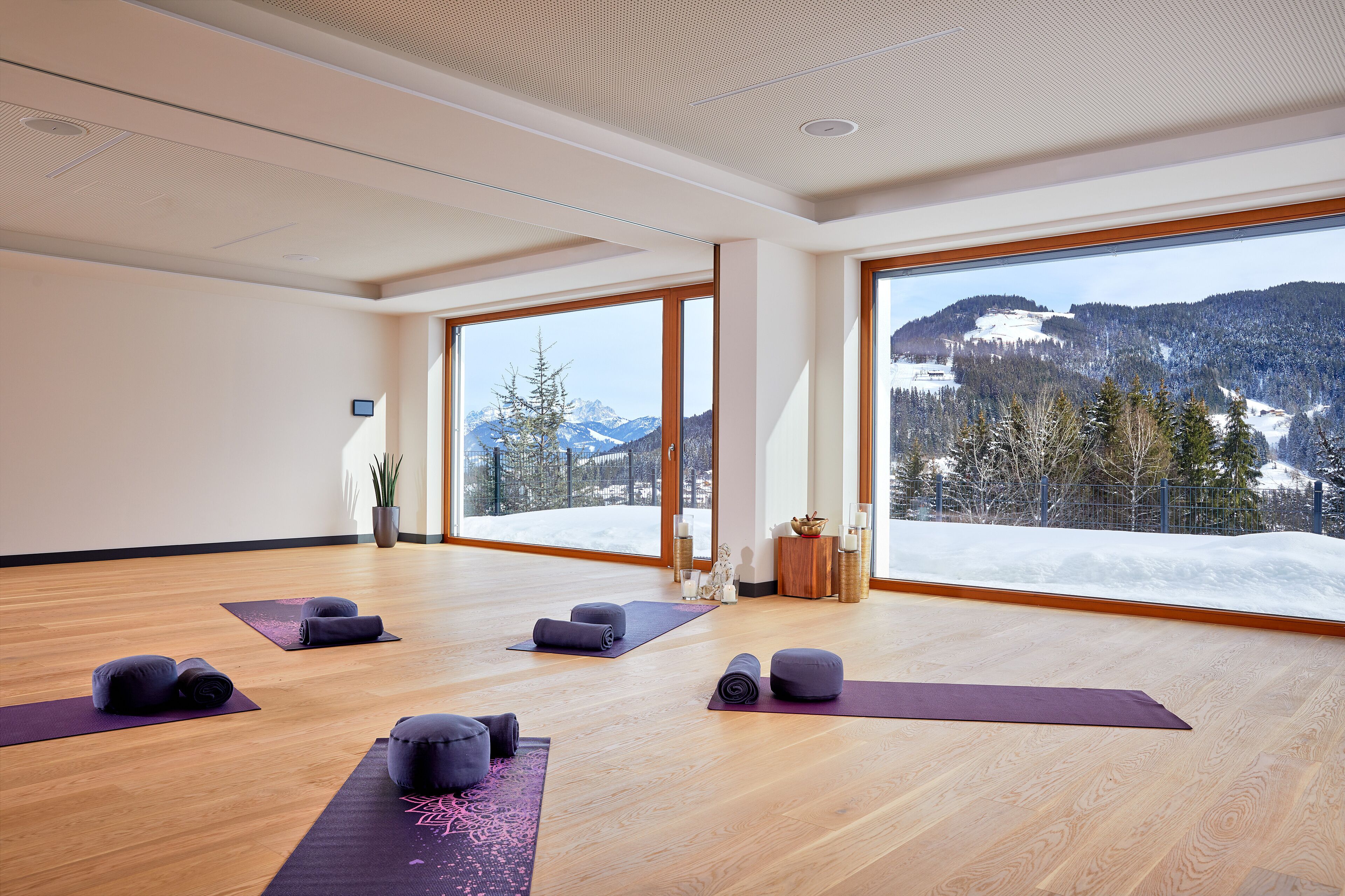 A spacious room with large windows, wooden flooring, and yoga mats arranged for use.