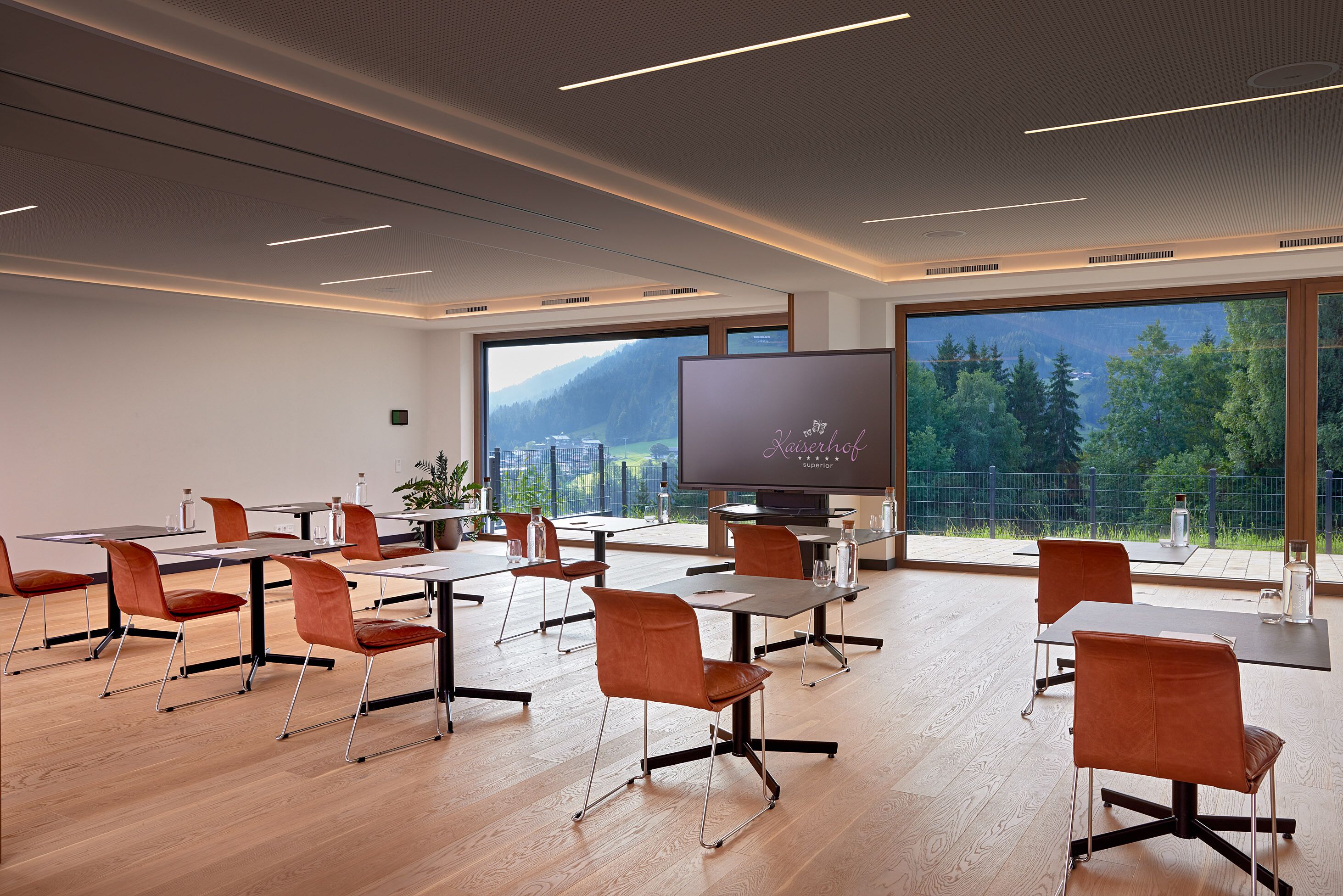 Un salón de conferencias con mesas y sillas, una pantalla grande y vistas a montañas a través de amplios ventanales.