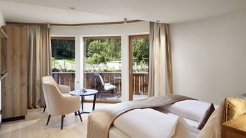 A hotel room with a large bed, a chair, a small table, and a balcony with a view of the outdoors.