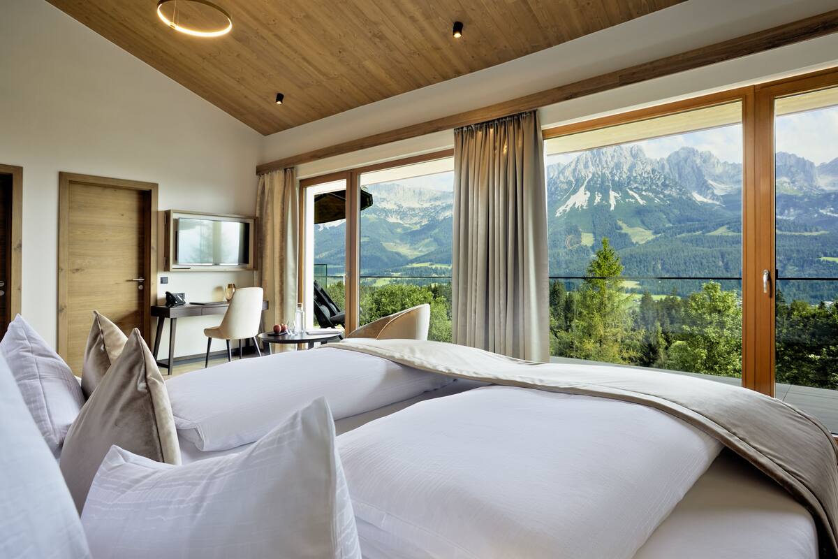 A hotel room with a large bed, a desk, and a view of mountains.