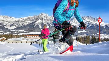 Une personne fait du ski sur une pente enneigée, avec une montagne en arrière-plan.