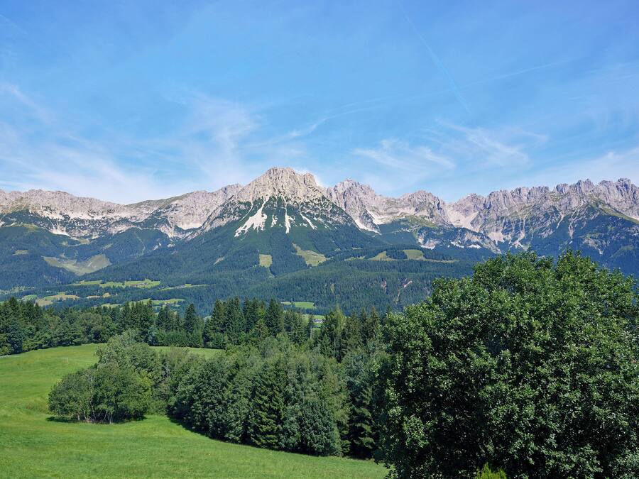 A mountain landscape with a prominent peak, lush green fields, and dense forests.