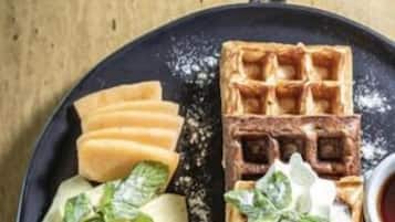 Une assiette contenant une gaufre, des tranches de pomme et des chips de banane.