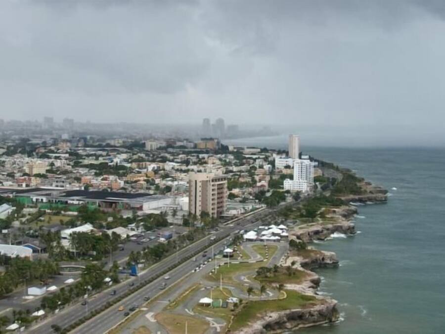 An aerial view of a coastal city with a prominent lighthouse, dense urban area, and a clear view of the sea.