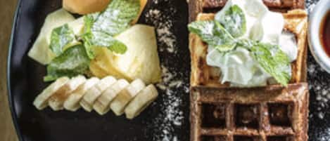 A plate with a waffle, banana slices, and a dollop of whipped cream.