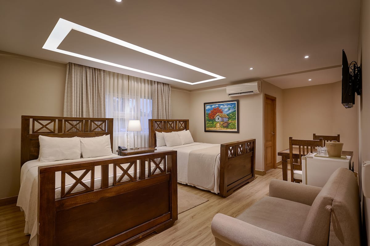 A hotel room with two wooden beds, a sofa, a desk, and a painting on the wall.