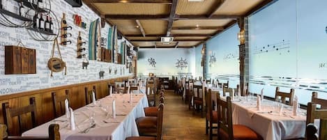 Un restaurante con mesas dispuestas para comer, una pared con nombres de ciudades y vistas a un cuerpo de agua.
