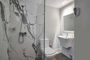 A modern bathroom with a glass-enclosed shower, a white toilet, and a built-in sink with a mirror above it.