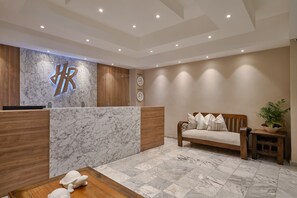 A reception area with a marble reception desk, wooden accents, a sofa, and a small table with a plant. - Hotel Riazor (Santo Domingo)