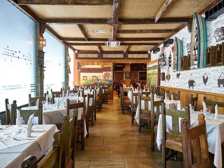 A restaurant with wooden tables and chairs, a tiled floor, and a high ceiling with exposed beams.