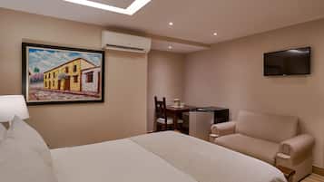 Quarto de hotel com cama, sofá, escrivaninha com cadeira, televisão e aparelho de ar condicionado.