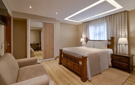 A bedroom with a bed, nightstands, a sofa, a wooden wardrobe, and a sliding door leading to a bathroom.