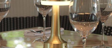 Una mesa con un candelabro de cristal, varias copas de vino y un tenedor sobre una superficie reflectante.
